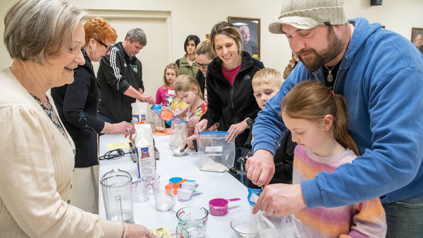 Andy Lang, right, and his daughter Sage, 8, both of Beaverton, place ingredients into a plastic bag to make dough for bread. Volunteer catechist Marabeth Holsinger, left, assists with the process for the Families Forming Disciples class on March 19. 